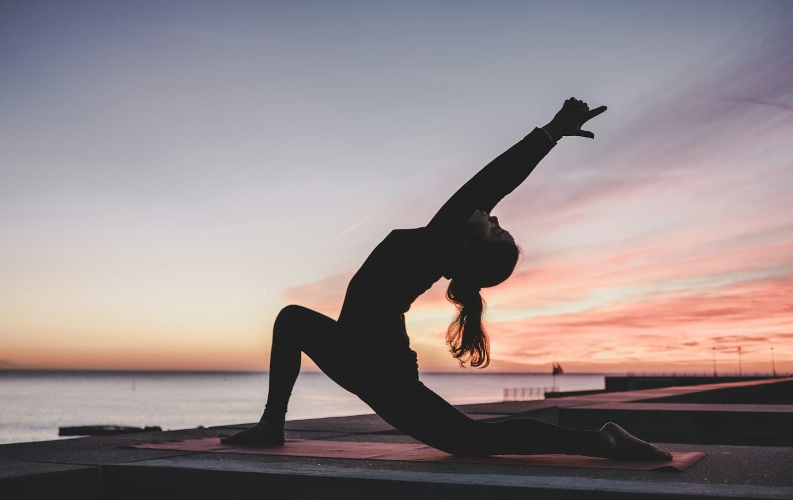 Silhouette of a person in a yoga stretch pose at sunset by the water